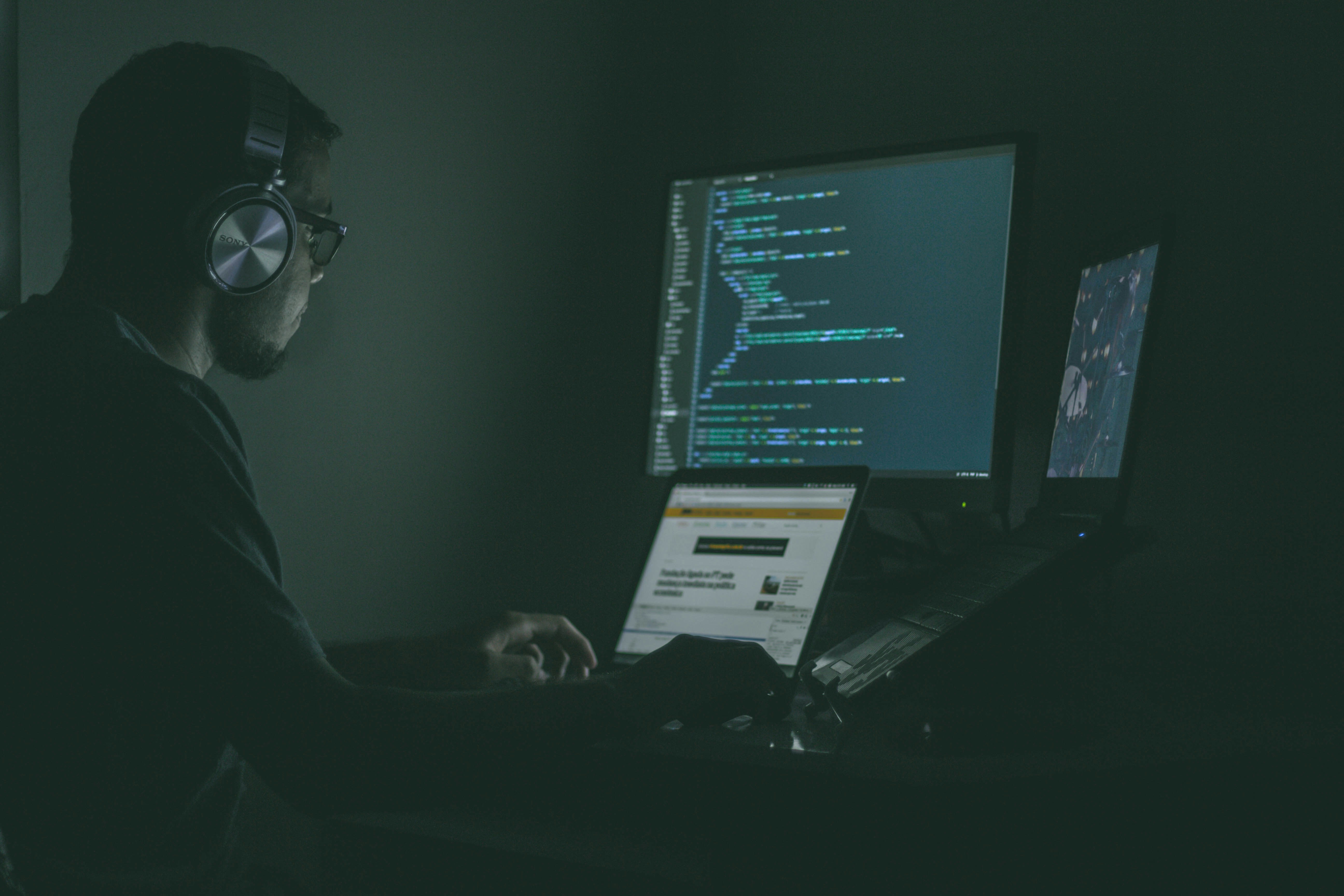 A person sits in front of a laptop, coding in a dimly lit room. A digital warning symbol flashes on the screen, representing a cyber threat targeting financial transactions in the private aviation industry.